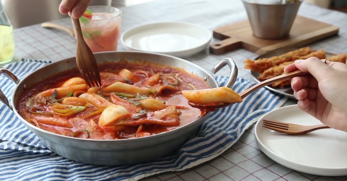 Tteokbokki cooking in a pan -- red gochujang sauce bubbling and thickening around rice cakes